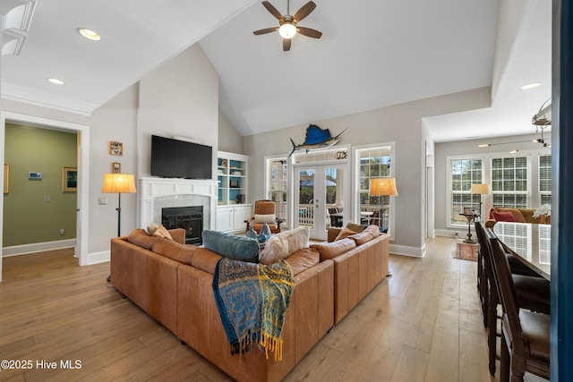 living room with baseboards, ceiling fan, light wood-style flooring, a fireplace, and high vaulted ceiling