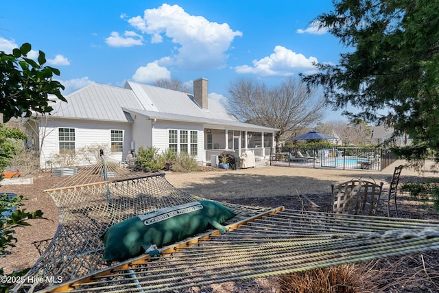 back of property with fence, a sunroom, metal roof, a chimney, and a patio area