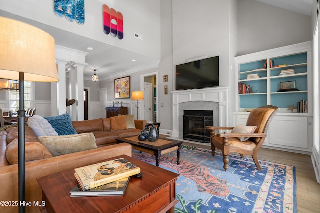 living room featuring visible vents, crown molding, a premium fireplace, a high ceiling, and wood finished floors