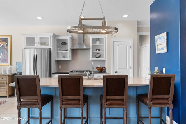 kitchen with backsplash, glass insert cabinets, wall chimney range hood, white cabinets, and stainless steel appliances