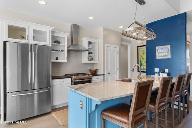 kitchen featuring wall chimney range hood, light wood-type flooring, decorative backsplash, appliances with stainless steel finishes, and a sink