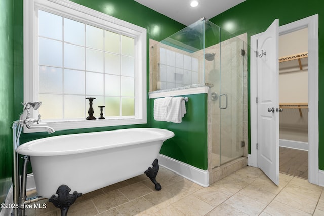 bathroom featuring a stall shower, a walk in closet, baseboards, and a freestanding tub