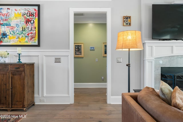 living area with a high end fireplace, visible vents, wainscoting, wood finished floors, and a decorative wall