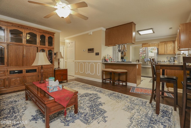 living room with a ceiling fan, ornamental molding, a textured ceiling, and wood finished floors