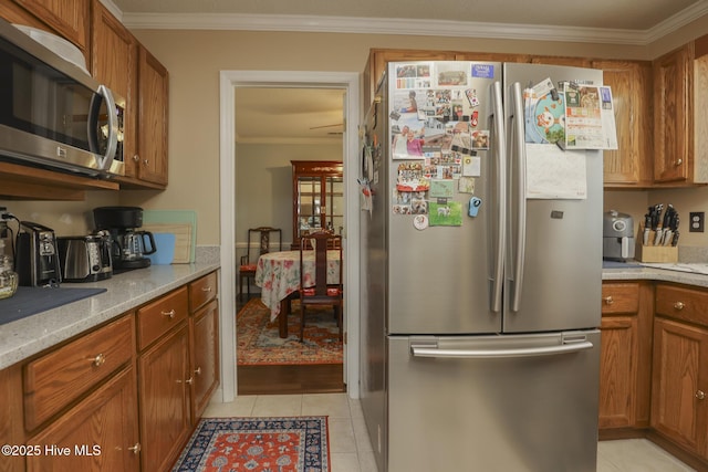 kitchen with appliances with stainless steel finishes, brown cabinets, ornamental molding, and light tile patterned floors