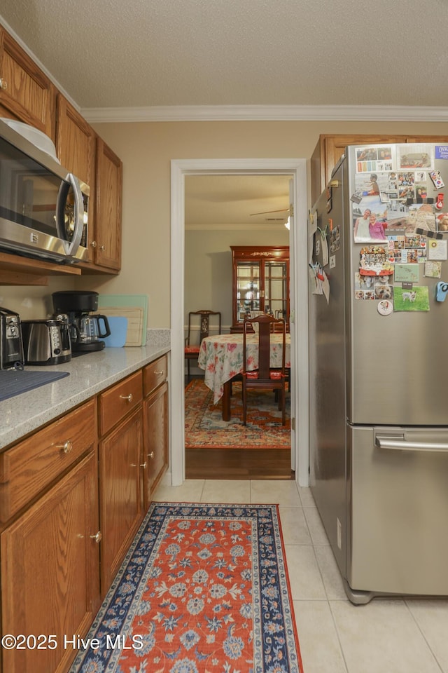 kitchen with light tile patterned floors, brown cabinetry, appliances with stainless steel finishes, a textured ceiling, and crown molding