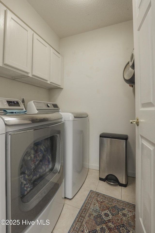 laundry room featuring cabinet space, light tile patterned floors, baseboards, a textured ceiling, and separate washer and dryer