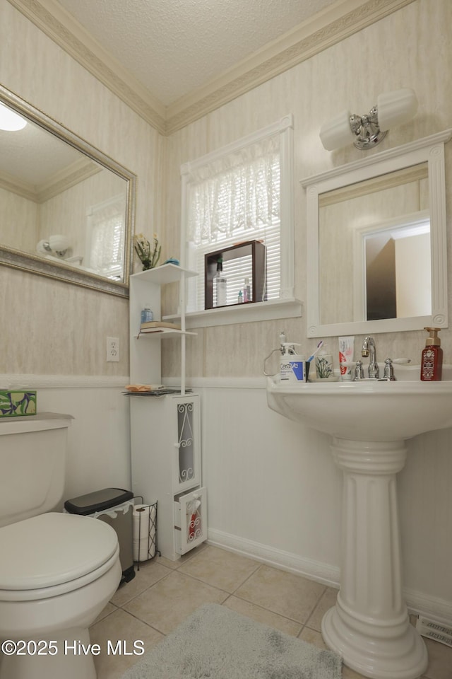 bathroom with toilet, ornamental molding, wainscoting, a textured ceiling, and tile patterned flooring