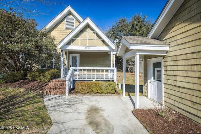 entrance to property featuring covered porch and roof with shingles