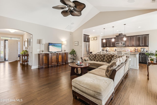 living room featuring ceiling fan, arched walkways, dark wood finished floors, and baseboards