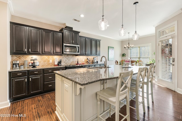 kitchen featuring a breakfast bar, decorative light fixtures, stainless steel microwave, a kitchen island with sink, and a sink