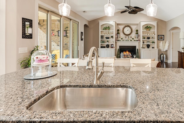 kitchen with arched walkways, light stone counters, a sink, open floor plan, and vaulted ceiling