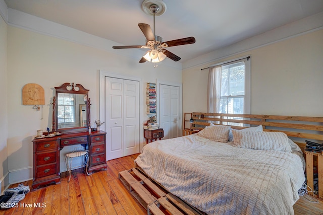 bedroom featuring multiple closets, light wood-type flooring, ornamental molding, and ceiling fan