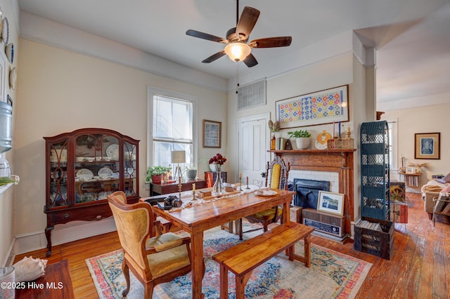 dining space with a ceiling fan, wood-type flooring, a fireplace, and baseboards