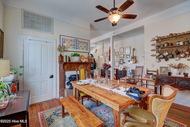 dining space featuring visible vents, ceiling fan, a fireplace, and wood finished floors