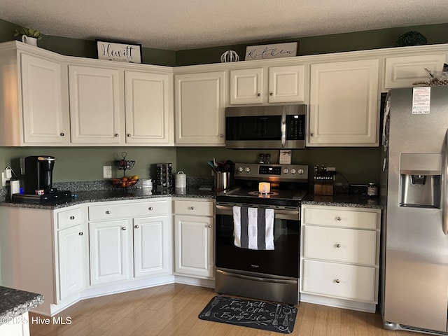 kitchen featuring appliances with stainless steel finishes, white cabinets, a textured ceiling, and light wood finished floors