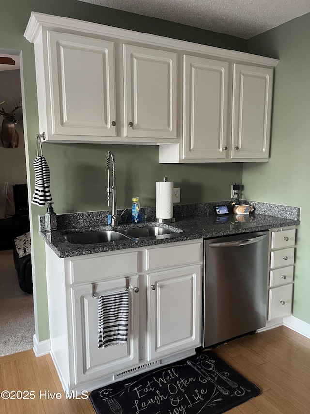 kitchen featuring dark stone counters, light wood-style flooring, stainless steel dishwasher, white cabinetry, and a sink