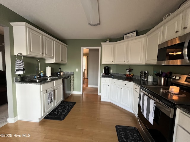 kitchen with white cabinets, light wood-style floors, stainless steel appliances, and a sink