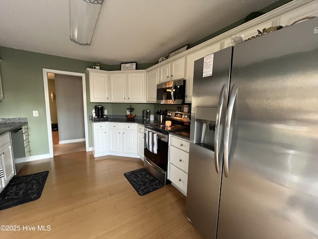 kitchen featuring stainless steel appliances, dark countertops, dark wood-type flooring, white cabinets, and baseboards