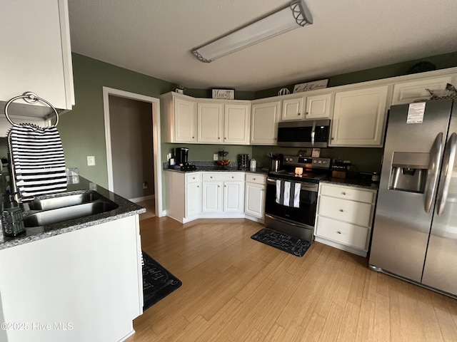 kitchen featuring stainless steel appliances, dark countertops, white cabinetry, and light wood-style flooring