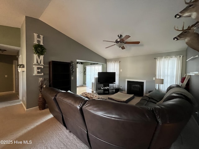 living area with a ceiling fan, a glass covered fireplace, light carpet, vaulted ceiling, and baseboards