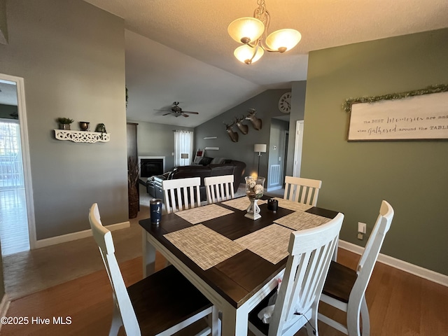 dining room featuring baseboards, vaulted ceiling, wood finished floors, and ceiling fan with notable chandelier