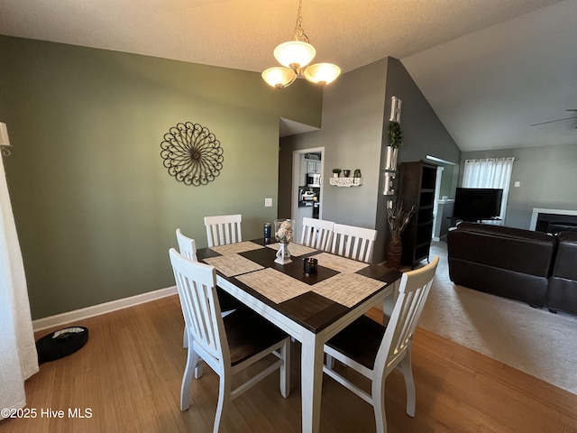 dining space featuring baseboards, vaulted ceiling, wood finished floors, and ceiling fan with notable chandelier