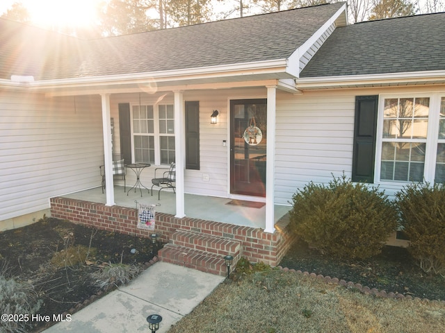 property entrance featuring covered porch and a shingled roof