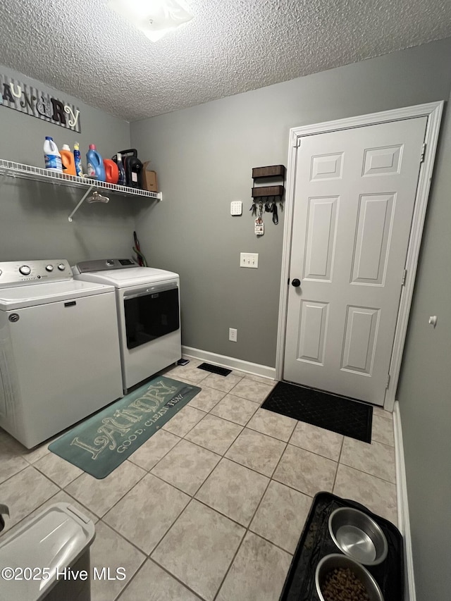 laundry area with laundry area, light tile patterned floors, a textured ceiling, and washing machine and clothes dryer