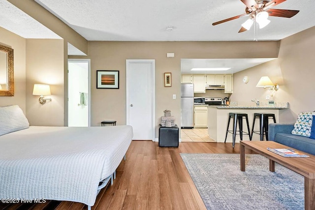 bedroom with a textured ceiling, light wood-type flooring, a sink, and freestanding refrigerator