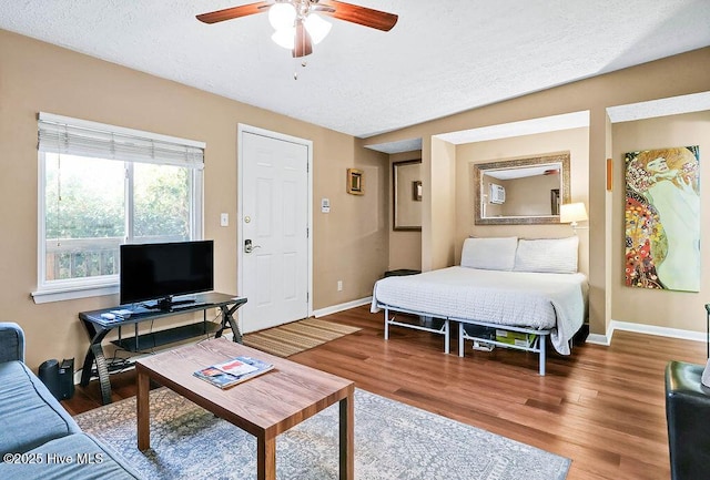 bedroom with a ceiling fan, a textured ceiling, baseboards, and wood finished floors