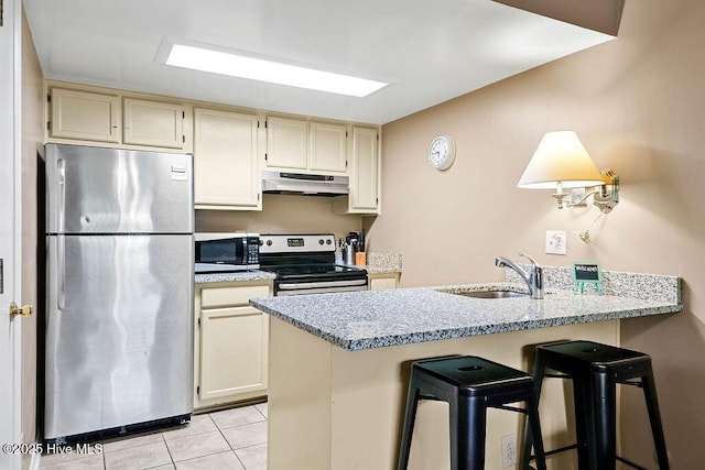 kitchen with light stone counters, under cabinet range hood, stainless steel appliances, a sink, and a kitchen breakfast bar