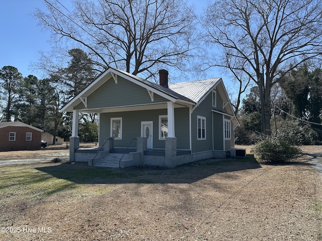 bungalow featuring covered porch, a chimney, and metal roof