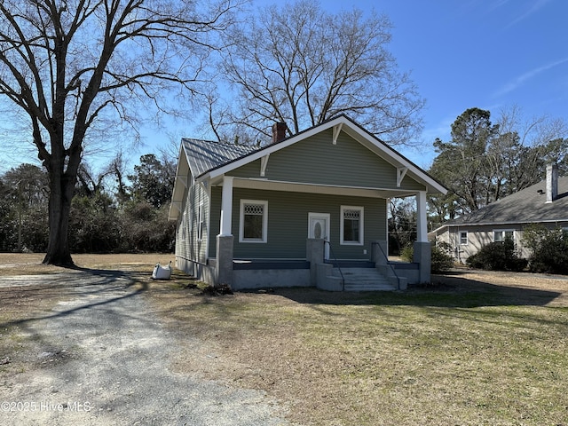 view of front facade with driveway, a chimney, metal roof, a porch, and a front yard