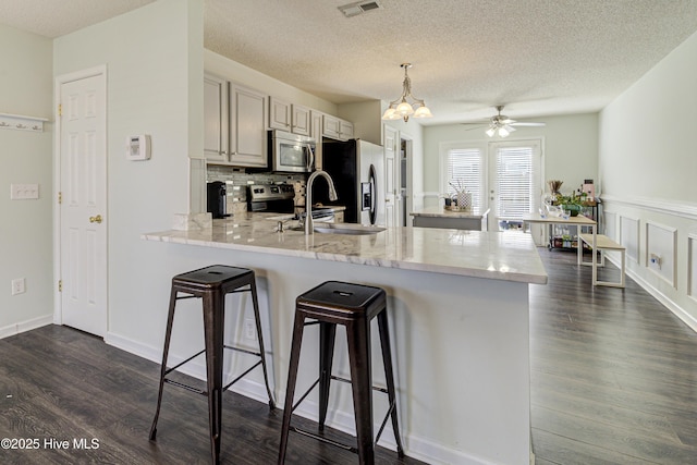 kitchen with stainless steel appliances, dark wood-type flooring, a peninsula, a sink, and a kitchen breakfast bar