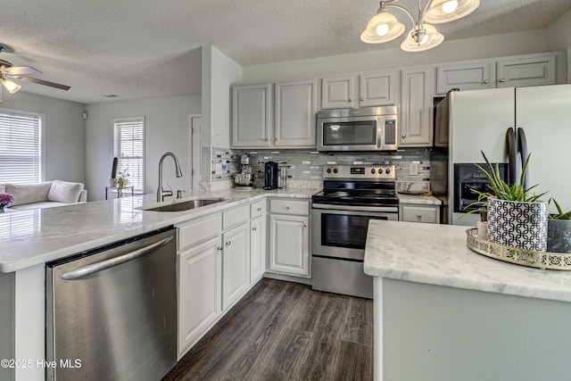 kitchen featuring stainless steel appliances, a peninsula, a sink, backsplash, and dark wood-style floors