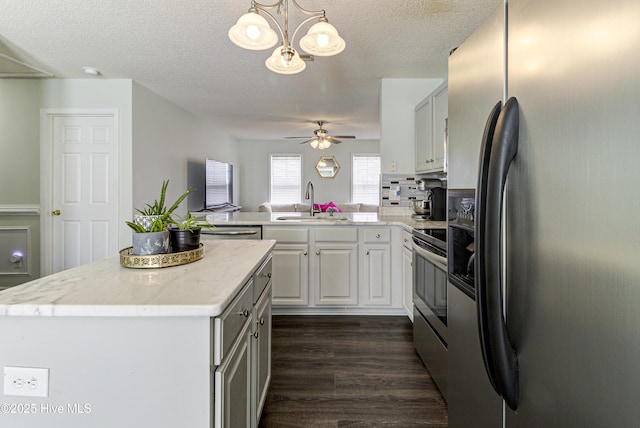 kitchen featuring stainless steel appliances, a peninsula, a kitchen island, a sink, and dark wood finished floors