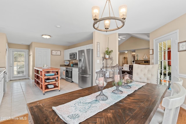 dining space with light tile patterned flooring, vaulted ceiling, and ceiling fan with notable chandelier