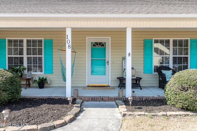 doorway to property with a shingled roof and a porch