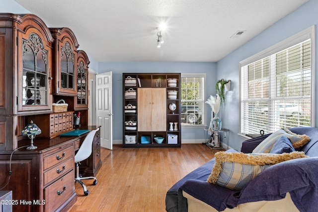 office area with baseboards, visible vents, a textured ceiling, and light wood finished floors