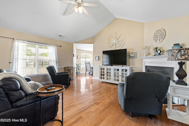 living area featuring a fireplace, lofted ceiling, light wood-style flooring, a ceiling fan, and baseboards