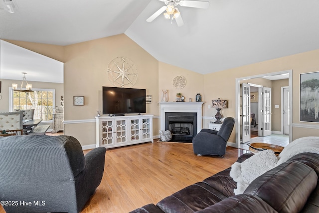 living area with a fireplace with flush hearth, vaulted ceiling, wood finished floors, baseboards, and ceiling fan with notable chandelier