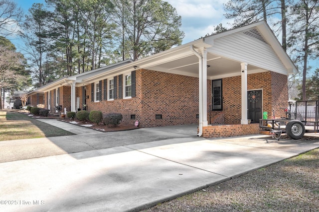 view of side of home with a carport, driveway, brick siding, and crawl space