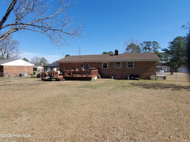 rear view of property with brick siding, a yard, a chimney, fence, and a wooden deck