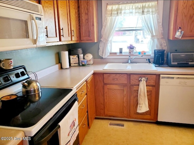 kitchen with brown cabinets, light countertops, visible vents, a sink, and white appliances