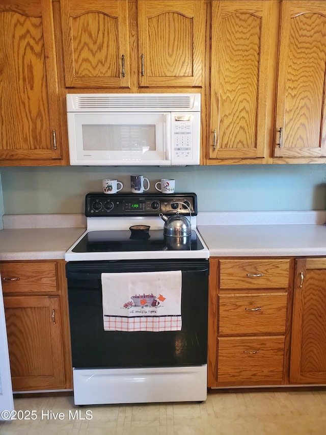 kitchen with electric range, light countertops, white microwave, and brown cabinets