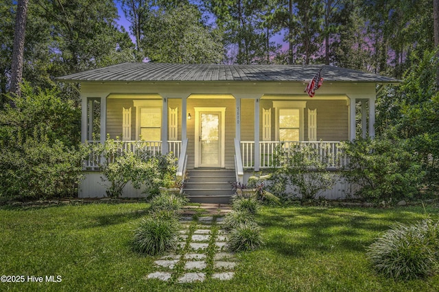 view of front facade with covered porch, metal roof, and a front lawn