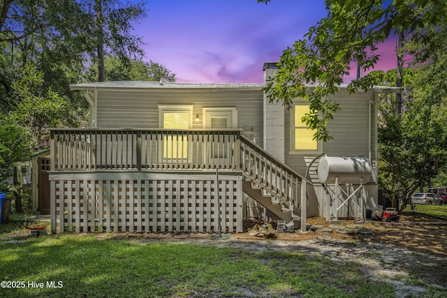 back of house at dusk featuring stairs and a wooden deck