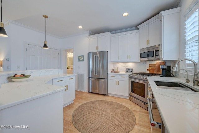 kitchen featuring premium appliances, a sink, white cabinetry, backsplash, and decorative light fixtures