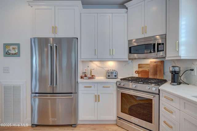 kitchen featuring stainless steel appliances, white cabinets, tasteful backsplash, and light stone counters